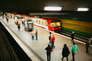 underground train station with a red train leaving and people walking on the platform.